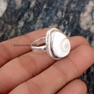 May include: A silver ring featuring a white, teardrop-shaped stone with a spiral design. The ring has a polished finish and is set in a simple, elegant band. The ring is shown on a hand.