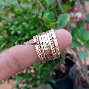 Puede incluir: Un conjunto de cinco anillos apilados en tono oro rosa con diversas texturas, incluyendo patrones de cuerda trenzada, una banda lisa con estrellas y lunas crecientes grabadas, y un motivo floral. El texto BalajiJewellersGifts es visible.