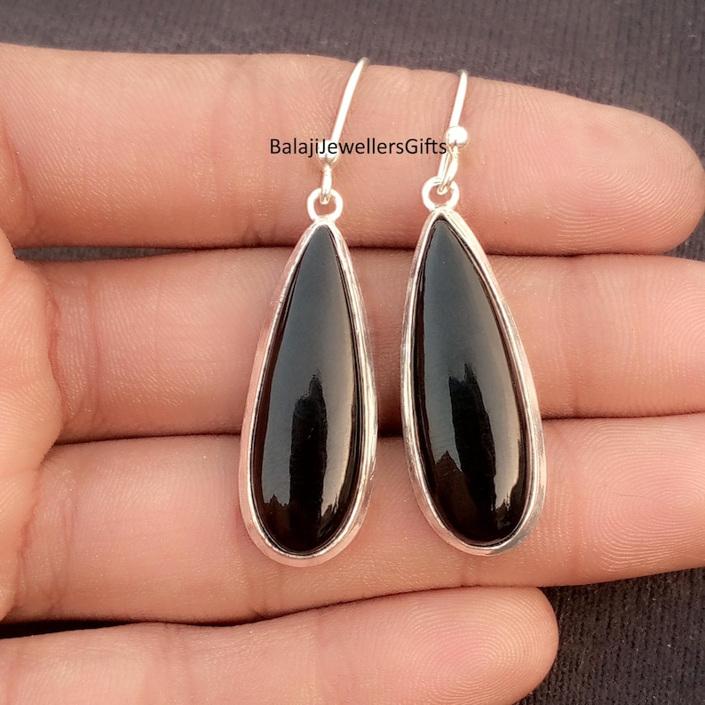 K&ouml;nnte beinhalten: Ein Paar tropfenf&ouml;rmige Ohrringe mit polierten schwarzen Steinen, eingefasst in silberfarbene Metallrahmen. Die Ohrringe haben einfache Haken f&uuml;r durchbohrte Ohren. Der Markenname "BalajiJewellersGifts" ist im Bild sichtbar.