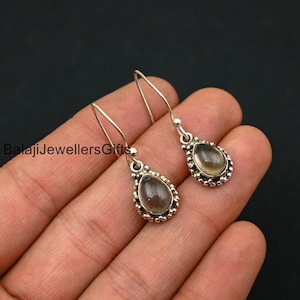 May include: A pair of silver dangle earrings with clear teardrop-shaped stones. The stones are set in a silver bezel with a beaded edge.