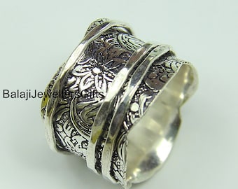 May include: A silver ring with a wide band featuring an intricate floral design. The band is textured and has a hammered finish.