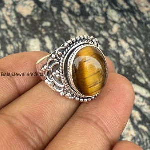 May include: A silver ring featuring an oval tiger's eye gemstone. The ring has an intricate, ornate design.