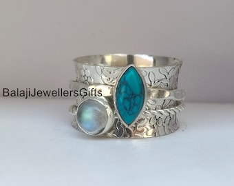 Peut inclure: Une bague tournante en argent avec une pierre turquoise et une pierre de lune. La bague est ornée d'un motif floral.