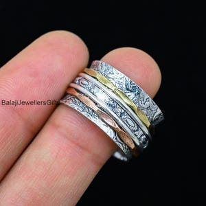May include: A silver spinning ring with multiple bands, each with a different pattern and texture. The bands are stacked on top of each other and spin freely. The ring is made of silver and has a gold band in the middle.