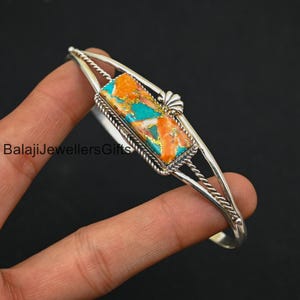 May include: A silver bracelet with a rectangular turquoise and orange stone set in a silver frame. The bracelet has a twisted wire design.