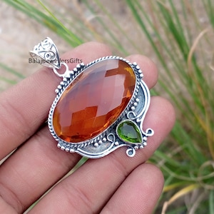Könnte beinhalten: Silberanhänger mit einem großen, facettierten, bernsteinfarbenen Edelstein. Der Anhänger hat einen kleineren, grünen, birnenförmigen Stein und dekorative Silberdetails. Der Text "BalajiJewellersGifts" ist sichtbar.