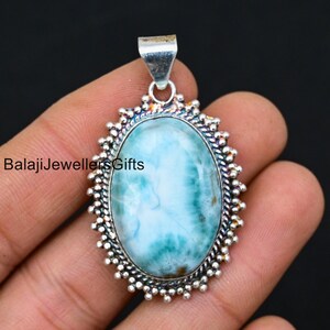 May include: A silver pendant with a large oval blue and green ocean jasper stone set in a silver bezel with a decorative border.  BalajiJewellersGifts is printed on the image.