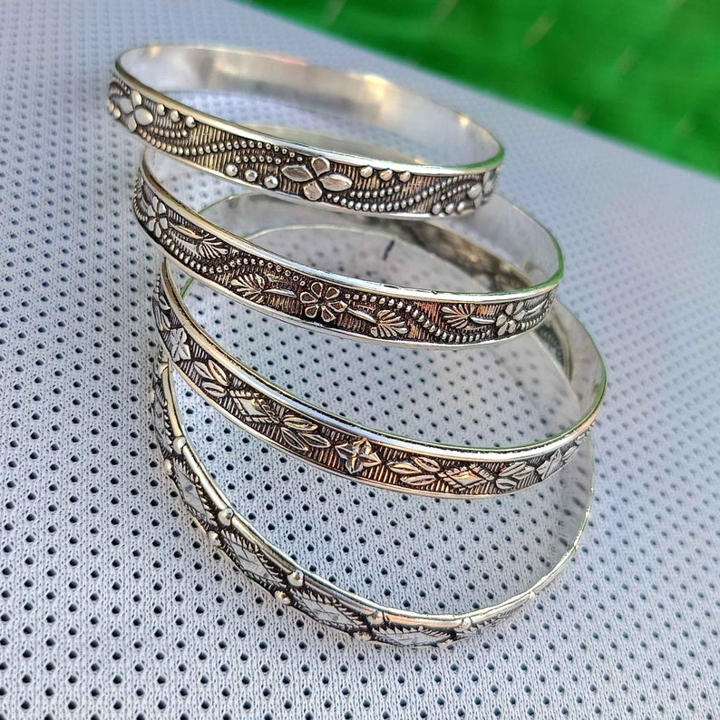 May include: Four silver bangles with floral designs. The bangles are stacked on top of each other.