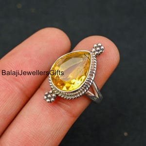 May include: A silver ring with a teardrop-shaped yellow gemstone set in a beaded bezel. The ring has a delicate band and a beaded design on the sides.