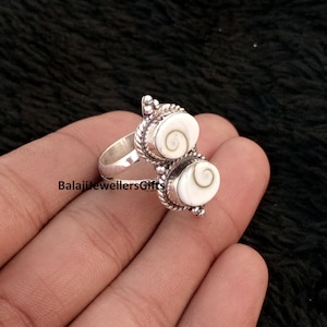Op de afbeelding: Een zilveren ring met twee ovale, witte en bruine schelpen stenen. De ring heeft een gedetailleerd, getextureerd ontwerp rond de stenen en band. De tekst "BalajiJewellersGifts" is zichtbaar.