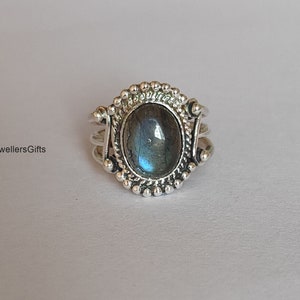 Pode incluir: Um anel de prata com uma pedra oval azul e cinza engastada em uma moldura de prata decorativa. O anel tem uma borda de contas e uma banda torcida.