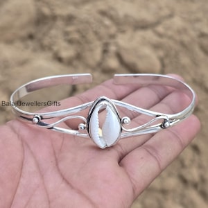 Könnte beinhalten: Ein silbernes Armreif-Armband mit einem weißen Muschelschmuckstück. Das Armband hat ein filigranes, offenes Design mit geschwungenen Linien und kleinen dekorativen Akzenten. Der Text "BalajiJewellersGifts" ist sichtbar.