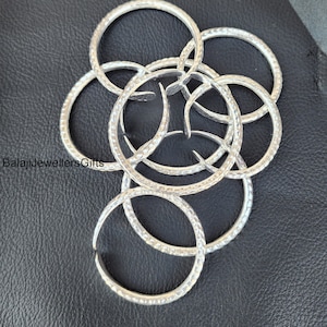 Puede incluir: Un conjunto de brazaletes de plata con textura martillada. Los brazaletes están apilados uno encima del otro y dispuestos en forma circular.