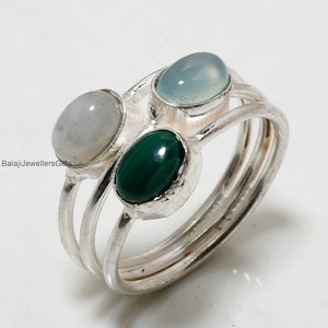 May include: A silver ring featuring three oval-shaped gemstones. The stones are a light blue chalcedony, a green malachite, and a white moonstone.