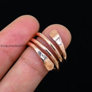 May include: A rose gold colored, multi-strand, spiral ring. The ring is made of thin, hammered metal.