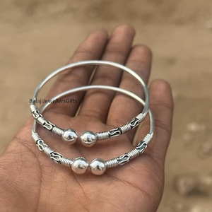 Op de afbeelding: Twee zilveren armbanden met decoratieve details en bolvormige accenten. De armbanden worden in een hand gehouden. De tekst "BalajiJewellersGifts" is zichtbaar op de afbeelding.