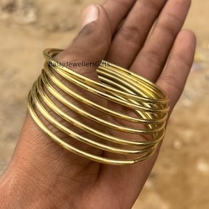 Könnte beinhalten: Ein Stapel goldfarbener Armreifen, gehalten in einer Hand. Die Armreifen sind dünn und rund, mit einer glatten, glänzenden Oberfläche. Der Text "BalajiJewellersGifts" ist auf dem Bild zu sehen.