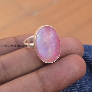 Op de afbeelding: Een zilveren ring met een grote ovale roze maansteen. De steen heeft een iriserende glans.