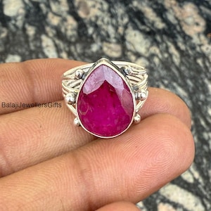 May include: A silver ring with a large, pear-shaped, pink ruby gemstone. The ring has a delicate, twisted band with small silver beads.