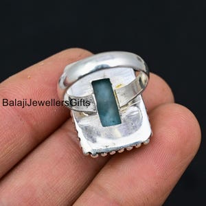 K&ouml;nnte beinhalten: Ein silberner Ring mit einem rechteckigen blauen Edelstein, der in einer silbernen Fassung sitzt. Der Ring hat einen perlenbesetzten Rand und ein glattes Band.