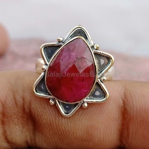 May include: A silver ring with a red ruby gemstone set in a star-shaped design. The ring is made of sterling silver and features a detailed design.