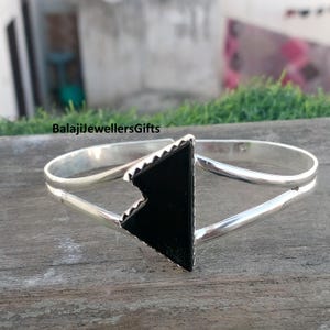 May include: A silver bracelet featuring a black triangular stone. The bracelet has a double-band design. The text "BalajiJewellersGifts" is visible in the image.