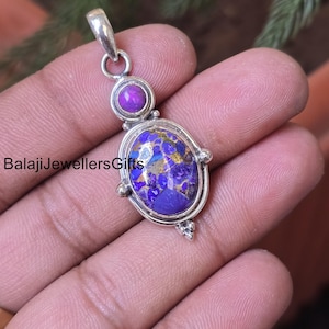 May include: A silver pendant with a purple and gold stone. The pendant has an oval-shaped stone with a silver border and a smaller round purple stone at the top. The text "BalajiJewellersGifts" is visible on the left side of the pendant.