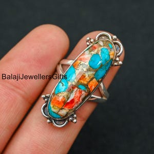 May include: A silver ring with an oval shaped turquoise and coral stone. The stone is a mix of blue, orange, and white.