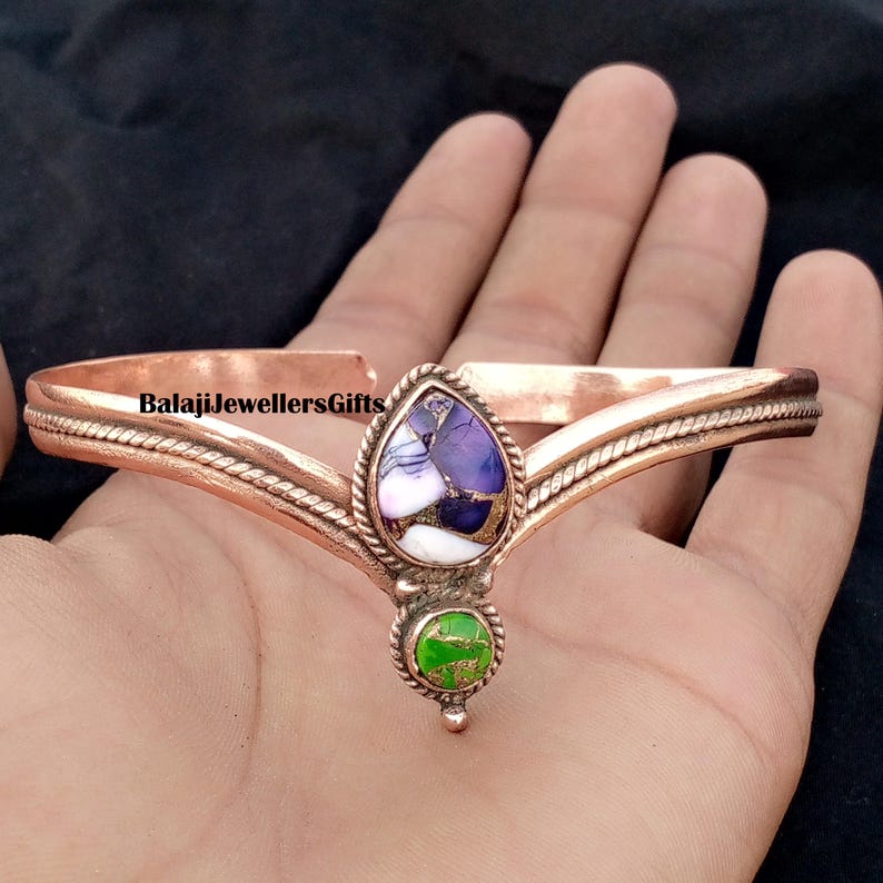 Op de afbeelding: Koperkleurige armband met een druppelvormige paarse en witte steen en een kleine groene steen. De armband heeft de tekst "BalajiJewellersGifts" erop.