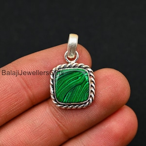 May include: A square pendant featuring a green malachite stone set in a silver frame with a rope design. The pendant is resting on a finger.