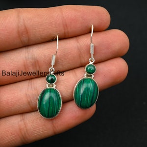 May include: A pair of silver earrings with green malachite stones. The earrings have a drop design with a smaller round stone at the top and a larger oval stone at the bottom.