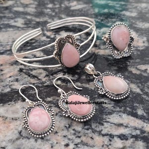 May include: A jewellery set comprising a silver bracelet, ring, pendant, and earrings. Each item features a teardrop-shaped, pale pink stone set in a decorative silver frame. The earrings are drop style.