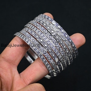Puede incluir: Un conjunto de nueve pulseras de plata con intrincados diseños geométricos. Las pulseras están apiladas una encima de la otra y tienen un acabado brillante.