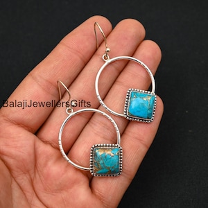 May include: A pair of silver hoop earrings with a turquoise stone set in a square frame. The hoops are textured and have a delicate design.