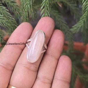 Könnte beinhalten: Ein Silberring mit einem großen, ovalen, hellrosa Edelstein. Der Edelstein ist in einem Silberband mit einem Kreuzmuster an den Seiten gefasst. Der Text "BalajiJewellersGifts" ist sichtbar.