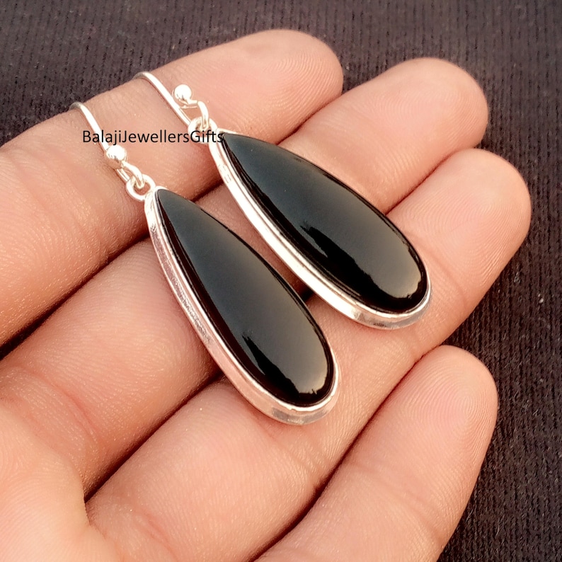 K&ouml;nnte beinhalten: Ohrringe zum H&auml;ngen mit tropfenf&ouml;rmigen schwarzen Onyxsteinen, gefasst in silberfarbenem Metall. Die Ohrringe haben ein schlichtes, elegantes Design mit poliertem Finish. Der Text "BalajiJewellersGifts" ist sichtbar.