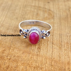 Może przedstawiać: Srebrny pierścionek z różowym owalnym kamieniem szlachetnym osadzonym w ozdobnej srebrnej oprawie. Pierścionek ma delikatny wzór z małymi srebrnymi koralikami i skręconym obrączką.