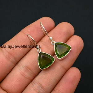 Może przedstawiać: Para srebrnych kolczyków wiszących z zielonymi trójkątnymi kroplami kamieni szlachetnych. Kolczyki mają prosty design i idealnie nadają się do codziennego noszenia.
