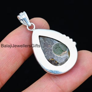 May include: Silver pendant featuring a teardrop-shaped setting with a green and brown ammonite fossil. The pendant has a bail for attaching to a chain.