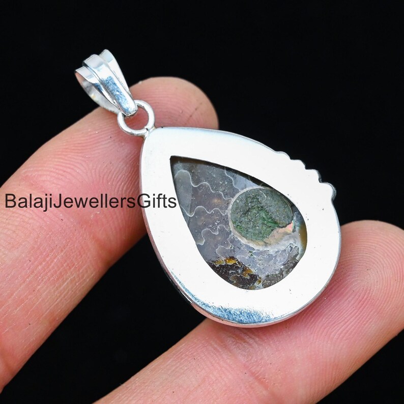 May include: Silver pendant featuring a teardrop-shaped setting with a green and brown ammonite fossil. The pendant has a bail for attaching to a chain.