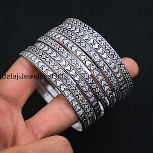 May include: A set of seven silver bangles with a heart and floral pattern. The bangles are stacked on top of each other.