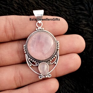 May include: A silver pendant featuring a large, round, pale pink rose quartz gemstone and a smaller, teardrop-shaped stone beneath. The pendant has an intricate silver setting. The text "BalajiJewellersGifts" is visible at the top of the pendant.