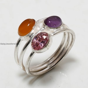 May include: A silver ring featuring three oval-shaped gemstones. The gemstones are orange, pink, and purple.