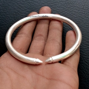 Könnte beinhalten: Ein silberfarbenes Armreif-Armband mit spitzen Enden. Das Armband ist rund und scheint aus Metall zu sein. Der Text "BalajiJewellersGifts" ist im Hintergrund sichtbar.