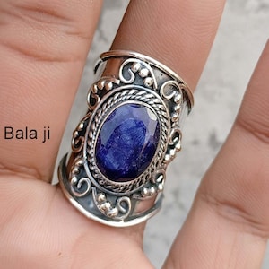 Könnte beinhalten: Ein silberner Ring mit einem ovalen, tiefblauen Edelstein. Der Ring hat ein verziertes Design mit Schnörkeln und Perlenakzenten. Der Text "Bala ji" ist sichtbar. Der Ring wird am Finger getragen.