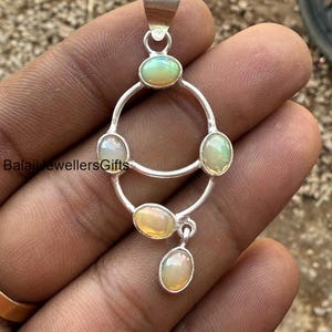 Puede incluir: Pendiente de plata con un diseño circular con cinco piedras preciosas de ópalo. El pendiente tiene un aro en la parte superior para sujetarlo a una cadena.
