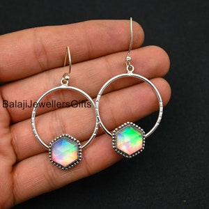 Peut inclure: Une paire de boucles d'oreilles créoles en argent avec une pierre précieuse hexagonale irisée au centre de chaque créole. Les boucles d'oreilles ont un délicat design perlé autour du bord de la créole et de la pierre précieuse.