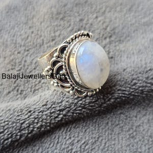 Könnte beinhalten: Ein silberner Ring mit einem großen ovalen Mondstein, der in einem filigranen Design eingefasst ist.