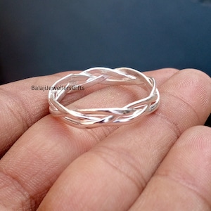 May include: A silver-colored ring with a braided design. The ring is made of a shiny metal and features a woven pattern. The ring is shown on a hand. The text "BalajiJewellersGifts" is visible.
