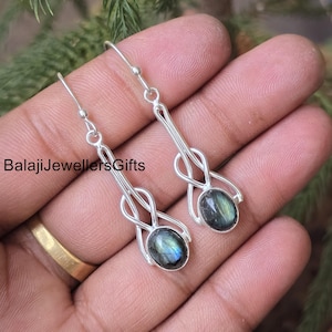 Può includere: Orecchini pendenti color argento con pietre preziose ovali e iridescenti. Gli orecchini hanno un design intrecciato unico e sono sospesi a un semplice gancio. Il testo "BalajiJewellersGifts" è visibile.
